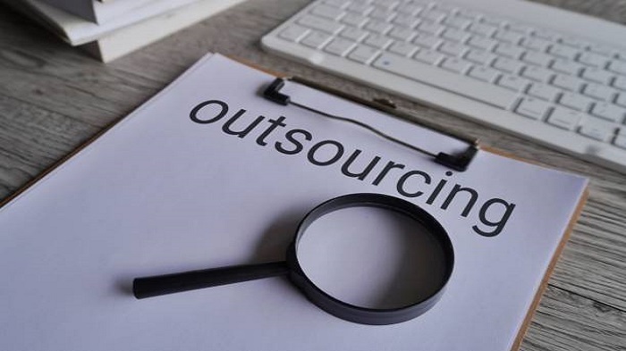 Gros plan sur une loupe et un presse-papiers avec le texte OUTSOURCING - externaliser sa paie à l'étranger - Activ Solution